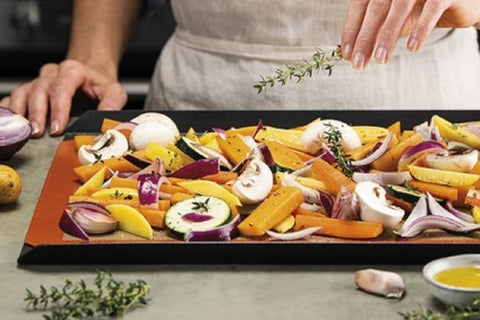 a woman using reusable baking mat to make veggies in the oven